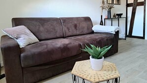 Un sofà de cuir marró amb un coixí blanc, una taula quadrada petita amb una planta en test i una taula auxiliar amb un vas i objectes decoratius.