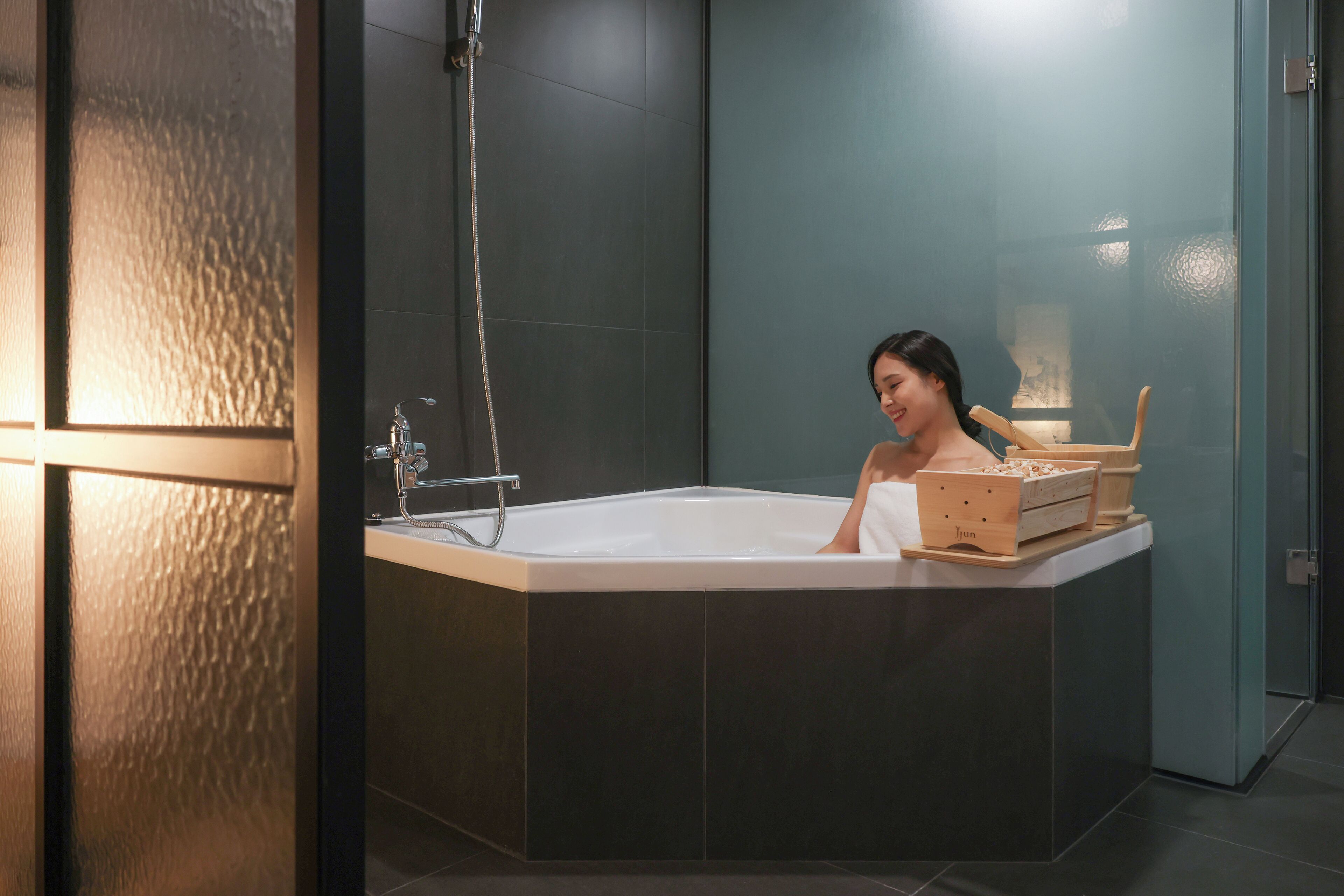 A modern bathroom with a freestanding bathtub, a glass shower enclosure, and a wooden side table with a towel and a box.