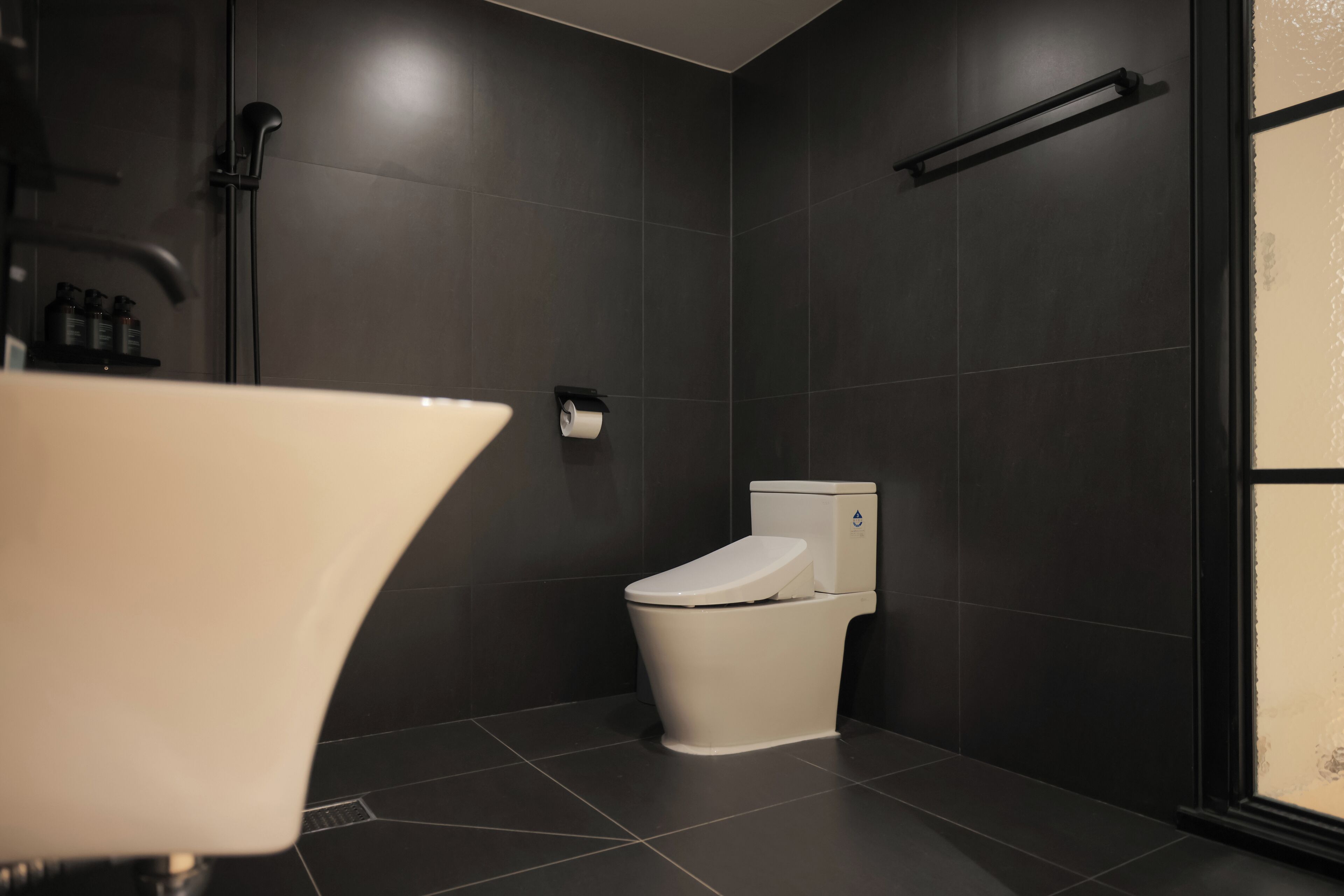 Et moderne badeværelse med toilet, håndklædestige og brusekabine i glas.