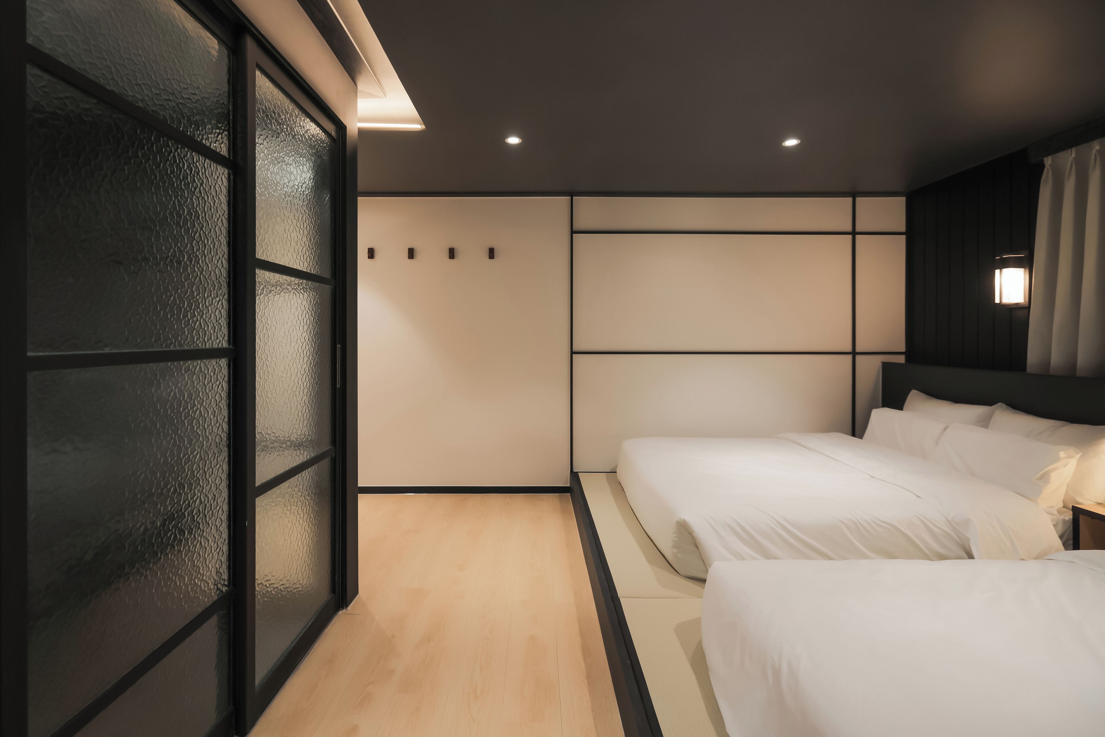 A modern bedroom with two beds, a sliding glass door, and recessed ceiling lighting.