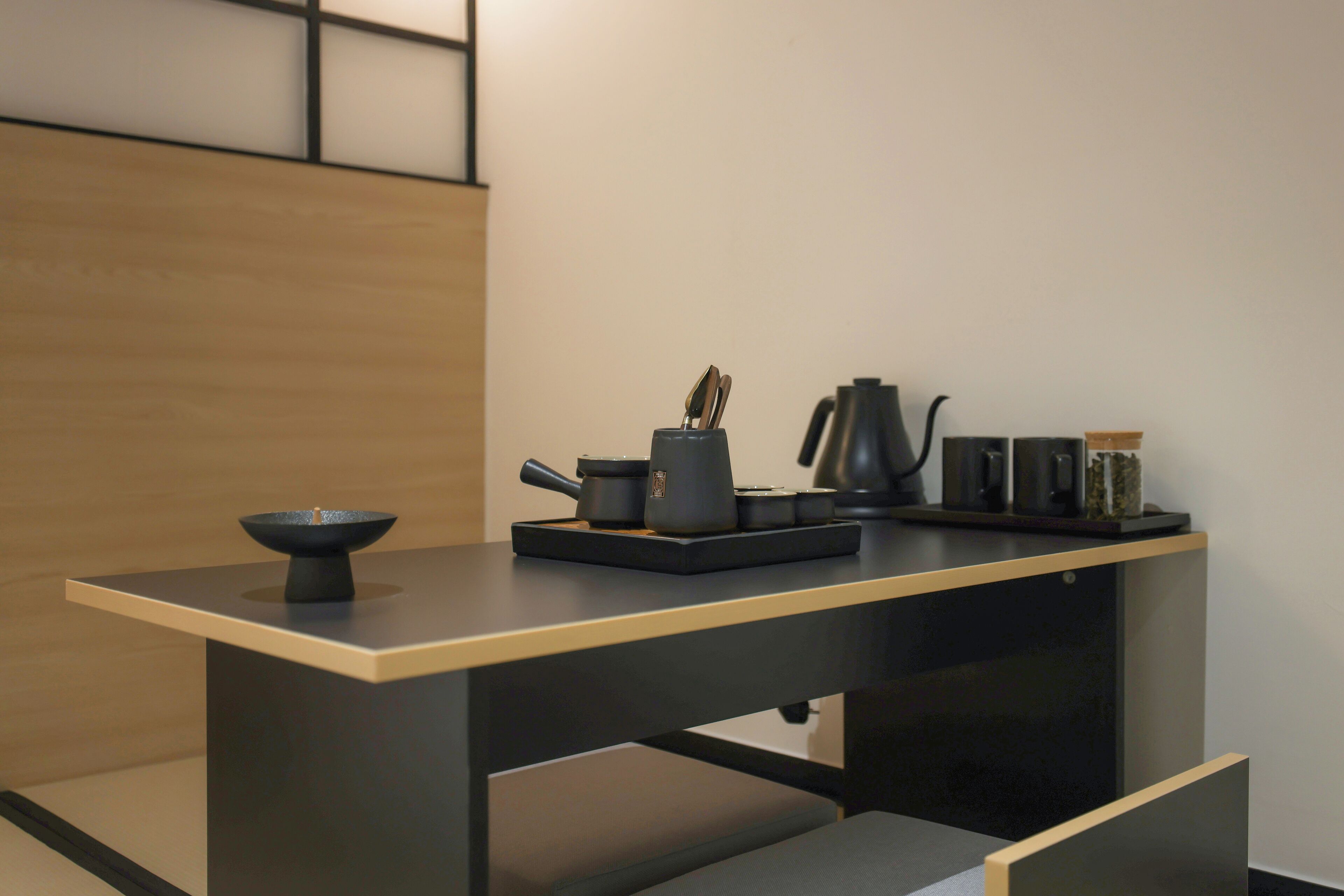 A modern kitchen with a minimalist design, featuring a dark countertop, a coffee maker, a kettle, and a bowl.