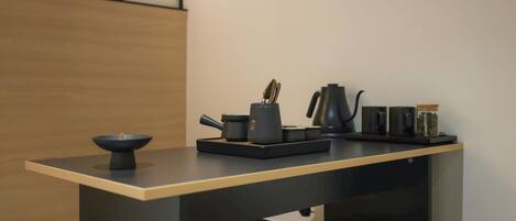 A modern kitchen with a minimalist design, featuring a dark countertop, a coffee maker, a kettle, and a bowl.