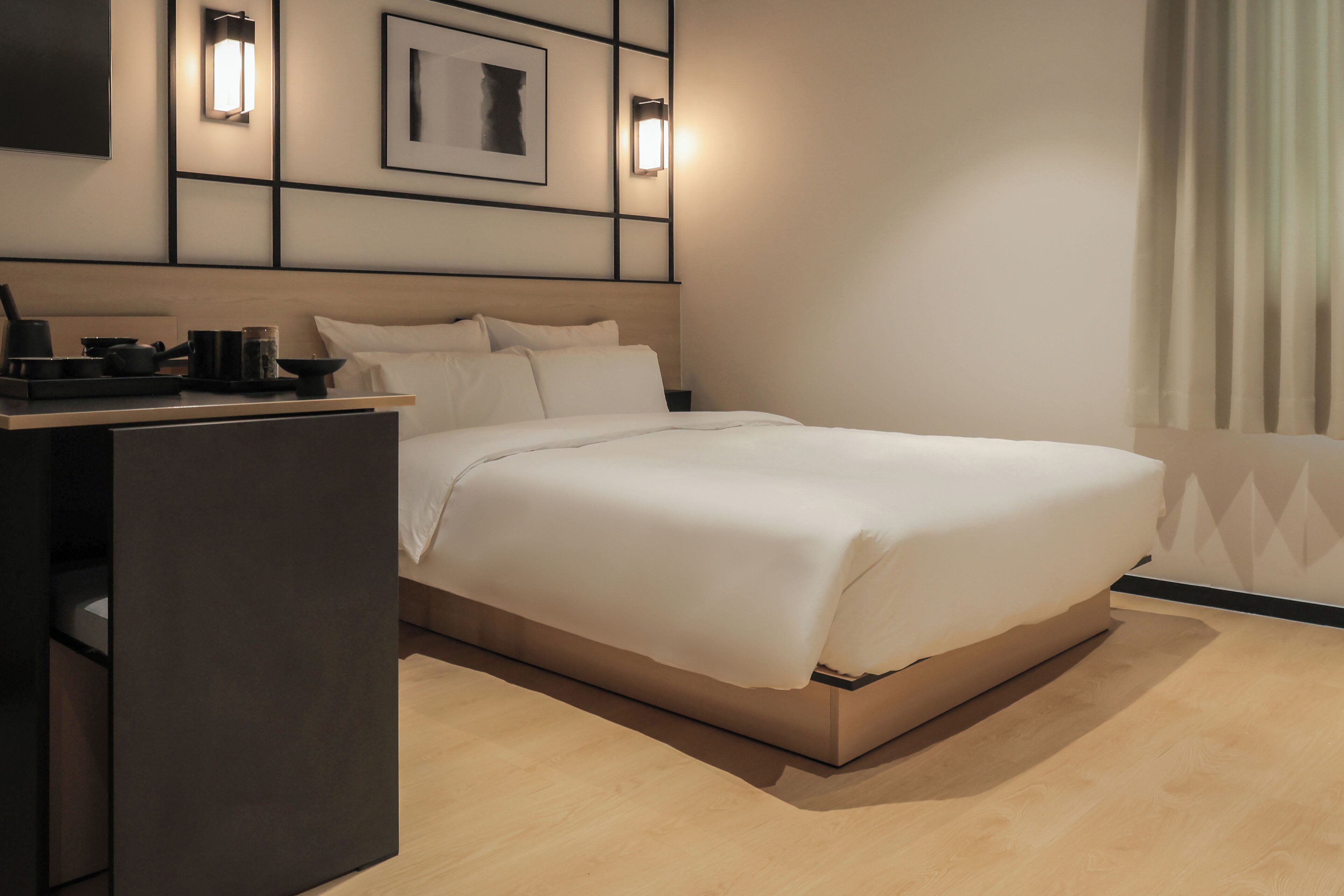 A modern hotel room with a bed, bedside table, and wall-mounted light fixtures.