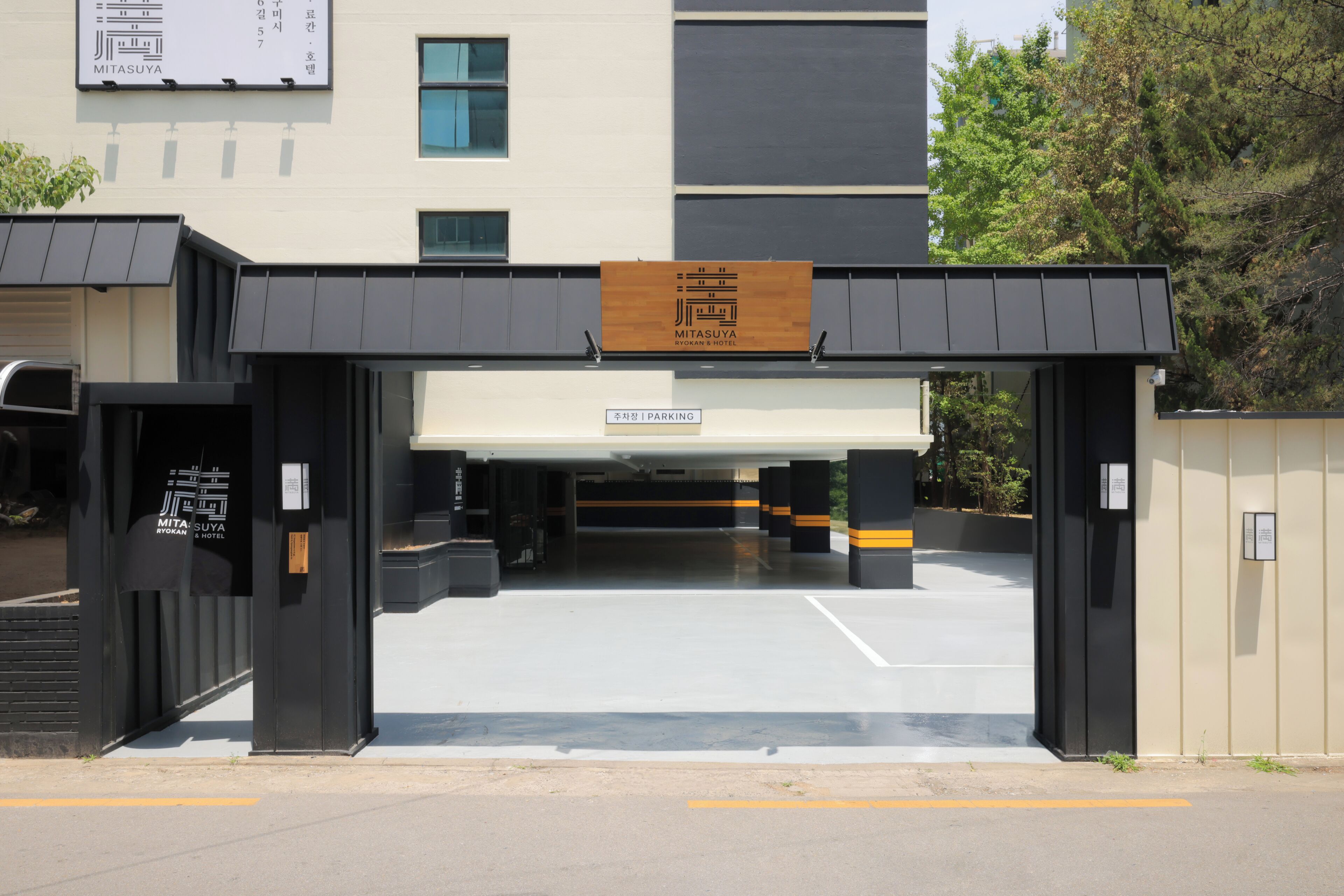 A hotel entrance with a signboard, a parking area, and a building facade.