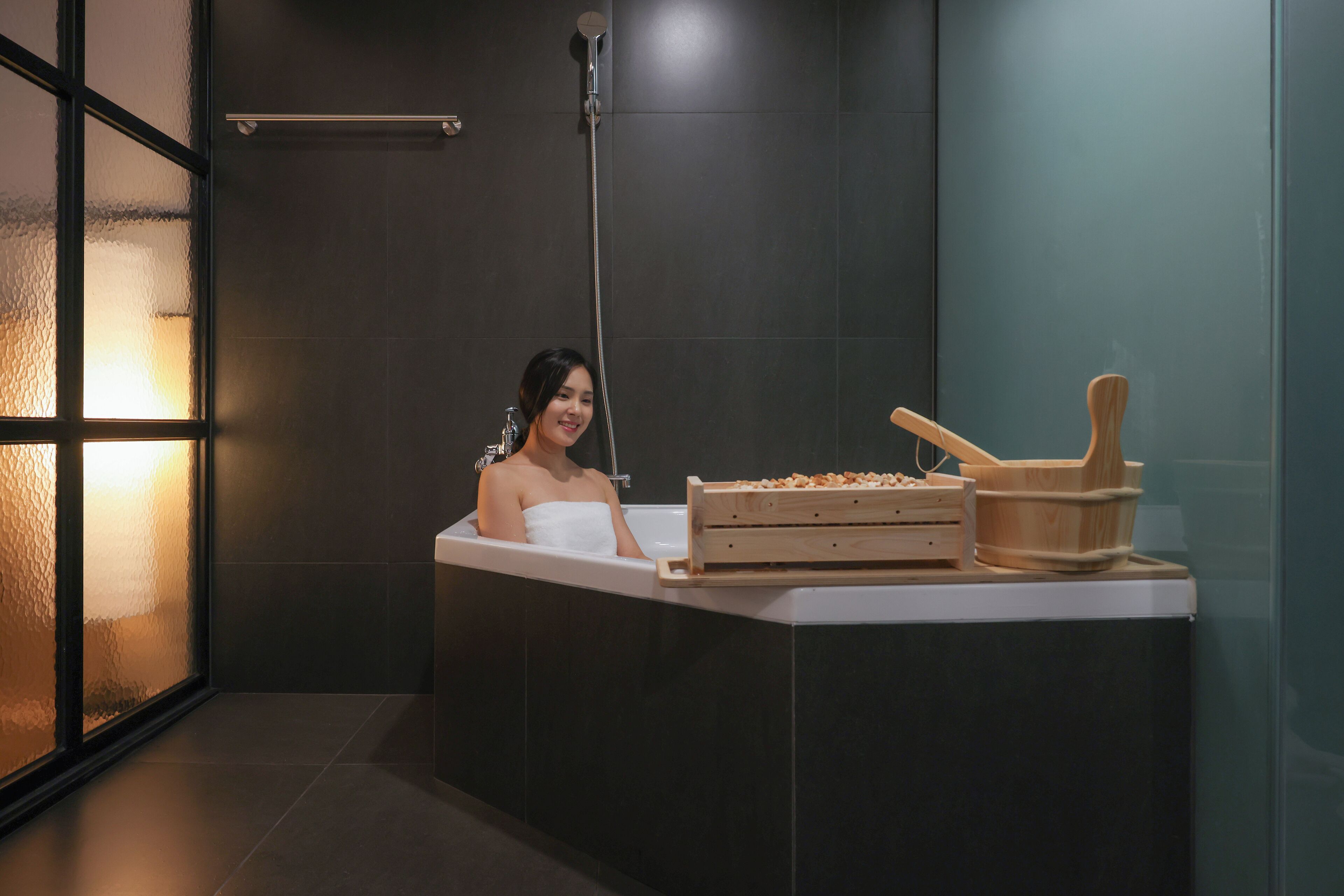 A modern bathroom with a bathtub, a wooden side table, and a glass shower enclosure.