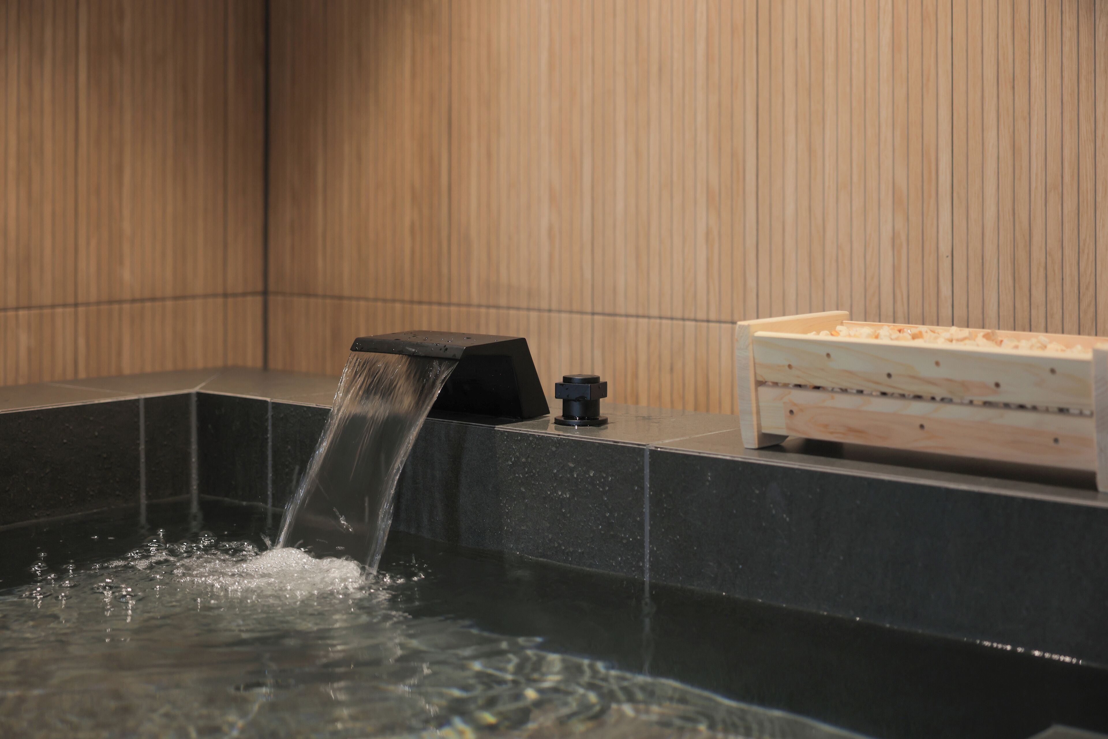 Un baño moderno con una bañera negra, un aparador de madera y una fuente de agua.