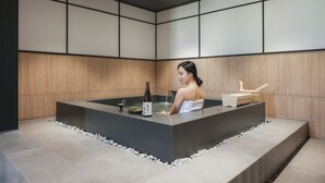 A spa room with a large bathtub, a bottle of sake, and a wooden bench. - Mitasuya Ryokan Hotel Gumi Wonpyeong Branch (Gumi)