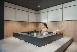 Un cuarto de spa con una bañera grande, una botella de sake y un banco de madera.