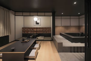 A modern interior with a long dining table, cushioned seating, a wall-mounted picture frame, and a built-in bathtub.