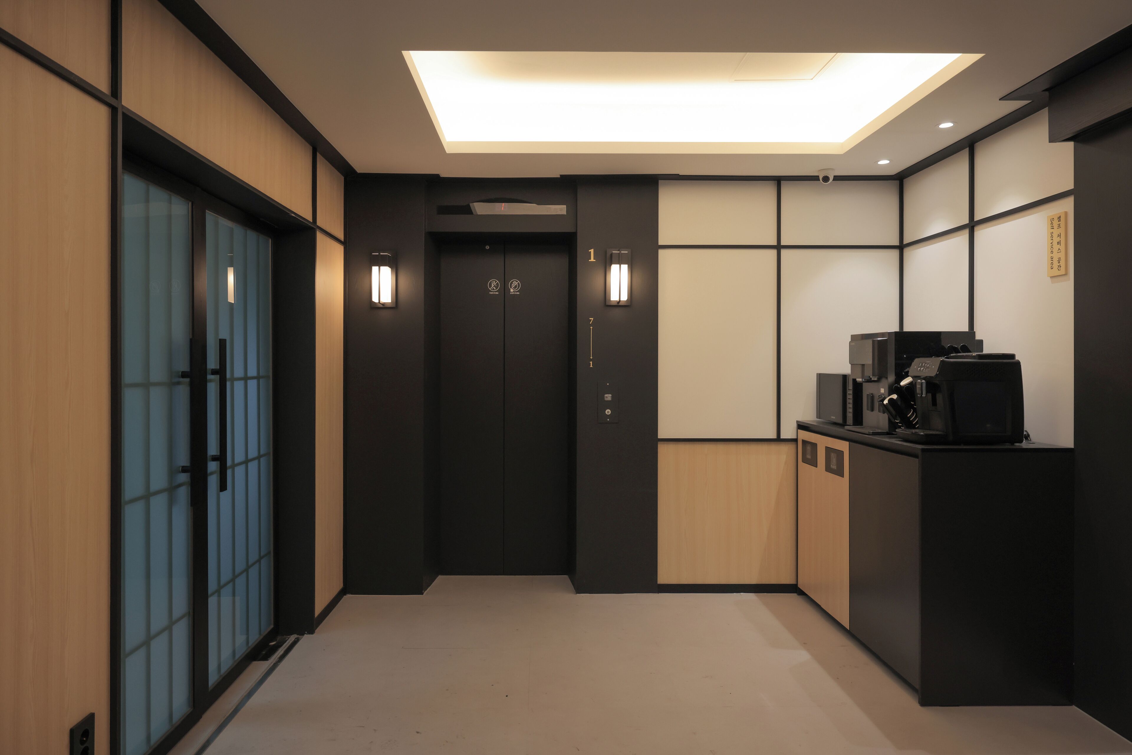 A modern elevator with a digital display, a reception area with a coffee machine, and a traditional sliding door.