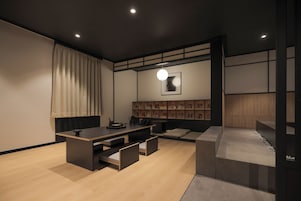 A modern living room with a wooden floor, a central seating area with cushions, a low table, and a wall-mounted shelf with framed pictures.