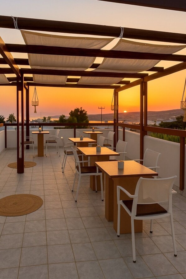 Una terraza con mesas y sillas, vistas al atardecer y una pérgola.