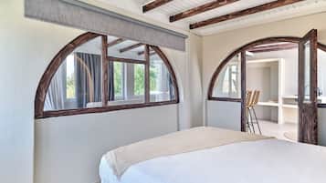 Une chambre dotée d’un grand lit, de poutres apparentes, de fenêtres en arc de cercle et offrant une vue sur l’extérieur.