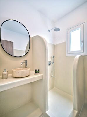 Un baño moderno con un espejo redondo, un lavabo color beige, una ducha y una ventana.