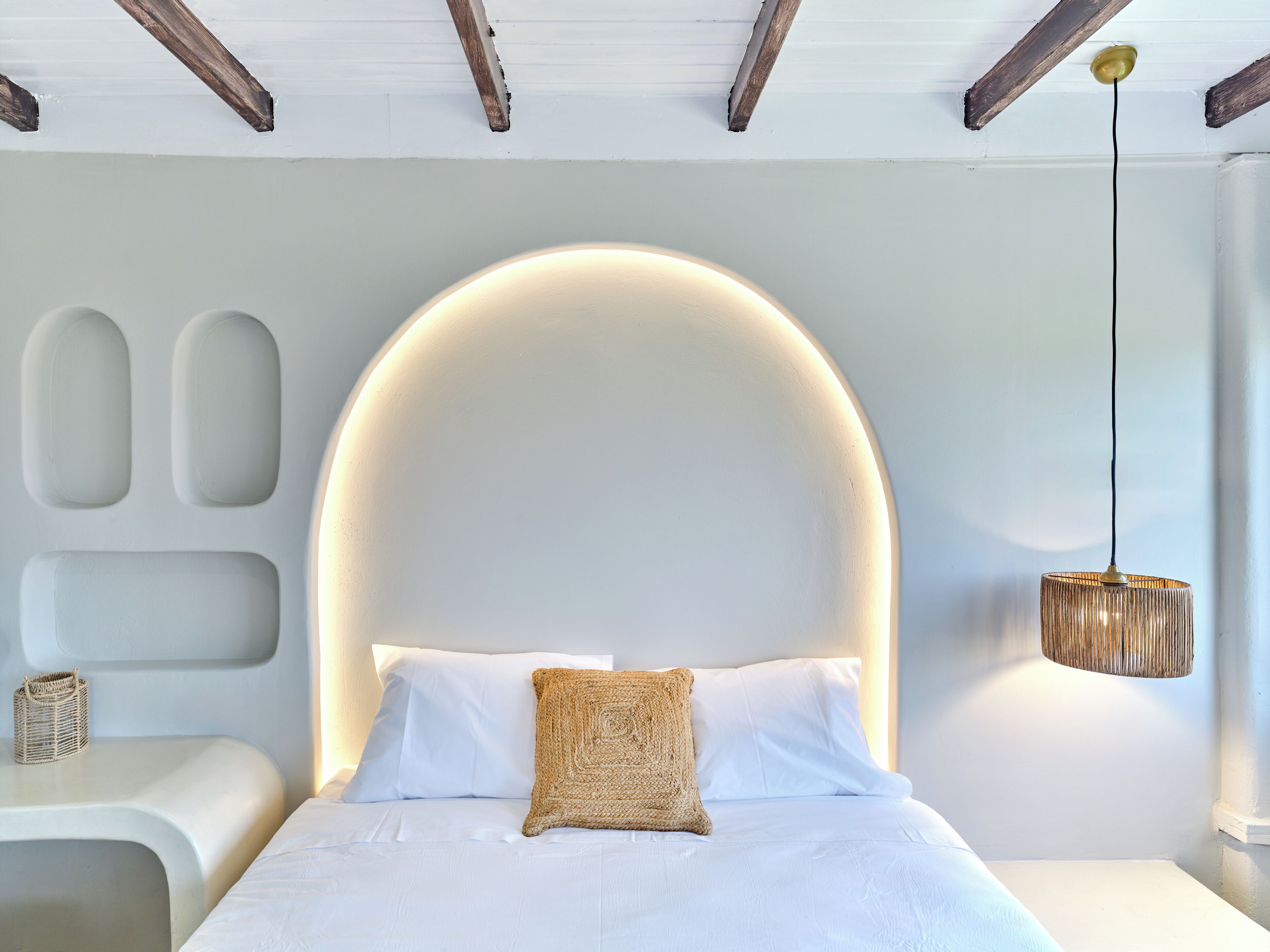 Un dormitorio moderno con una cabecera curvada, una mesita de noche con una cesta tejida y una lámpara colgante.
