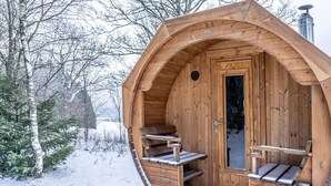 A wooden cabin with a curved roof, a door, and a small porch with benches.