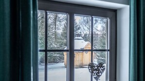 A window with a view of a wooden cabin in a snowy landscape.