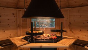 A wood-paneled room with a central grill station featuring multiple cooking surfaces and a chimney.