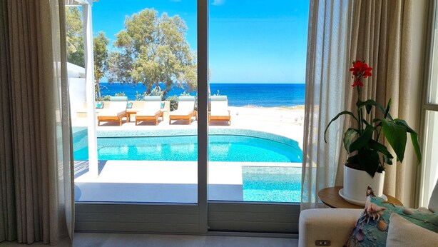 A room with a view of a swimming pool, lounge chairs, and a beach.