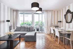 Una sala de estar moderna con un sofá seccional gris, una mesa de comedor con sillas y un ventanal con cortinas.