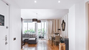 A modern living room with a sofa, dining table, and chairs. There is a large window with curtains, a hanging light fixture, and a potted plant. - Easylife - Splendid flat with balcony Central FS (Milano)