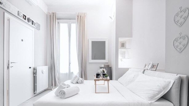 Ein modernes Schlafzimmer mit einem großen Bett, einem Nachttisch, einem Heizkörper und einem Fenster mit Vorhängen.