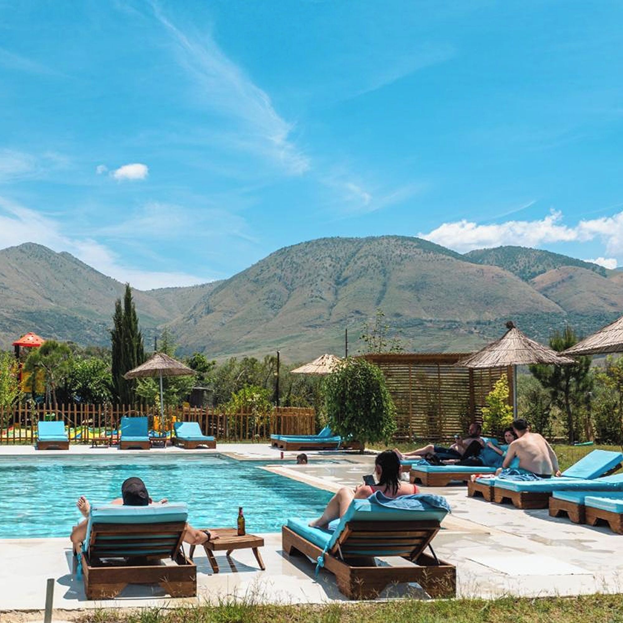 A poolside area with lounge chairs and umbrellas, surrounded by mountains.