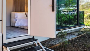 A modern mobile home with a bedroom featuring a bed, curtains, and a window. - Mesopotam Agrotourism Resort (Mesopotam)