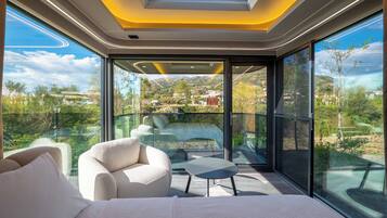 A modern room with a bed, a sofa, a small table, and a glass wall offering a scenic view.