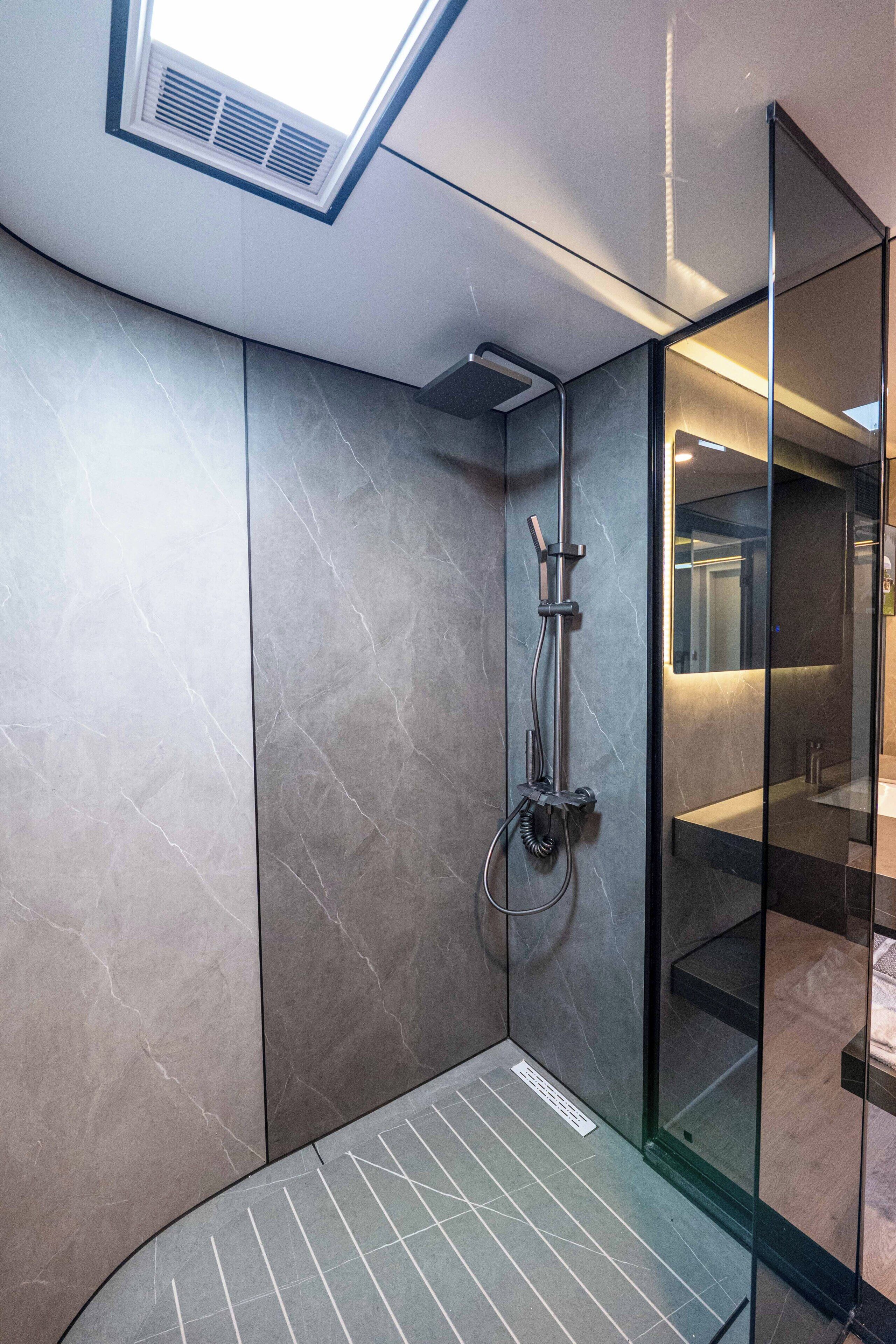 Un baño moderno con cabina de ducha de vidrio, tragaluz y suelo de mármol.