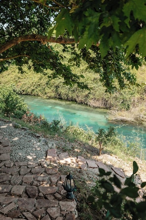 A stone pathway leading to a river with clear water, surrounded by greenery and trees. - Mesopotam Agrotourism Resort (Mesopotam)