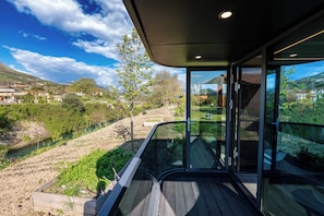 Un bâtiment moderne doté de grandes fenêtres en verre, d’une terrasse en bois et offrant une vue sur une rivière et les environs.