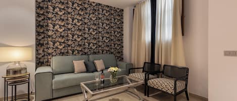 A living room with a sofa, a glass coffee table, a patterned wall, a lamp, and a chair.