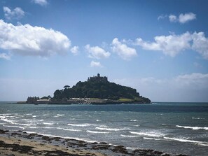 A coastal view with a castle on a hill, beach, and ocean waves. - Eco-friendly Cornish Sanctuary Peaceful Location (Penzance)