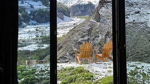 Une vue sur la montagne, depuis une fenêtre, avec deux fauteuils Adirondack en bois.