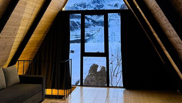 Une pièce aux hauts plafonds, avec des poutres en bois et une grande fenêtre donnant sur une montagne enneigée.