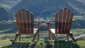 Deux fauteuils Adirondack en bois, placés face à un paysage pittoresque d’une vall ée avec des montagnes en arrière-plan.