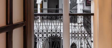 Um amplo salão com lustre, grades de ferro ornamentadas e vista para um edifício com varandas.