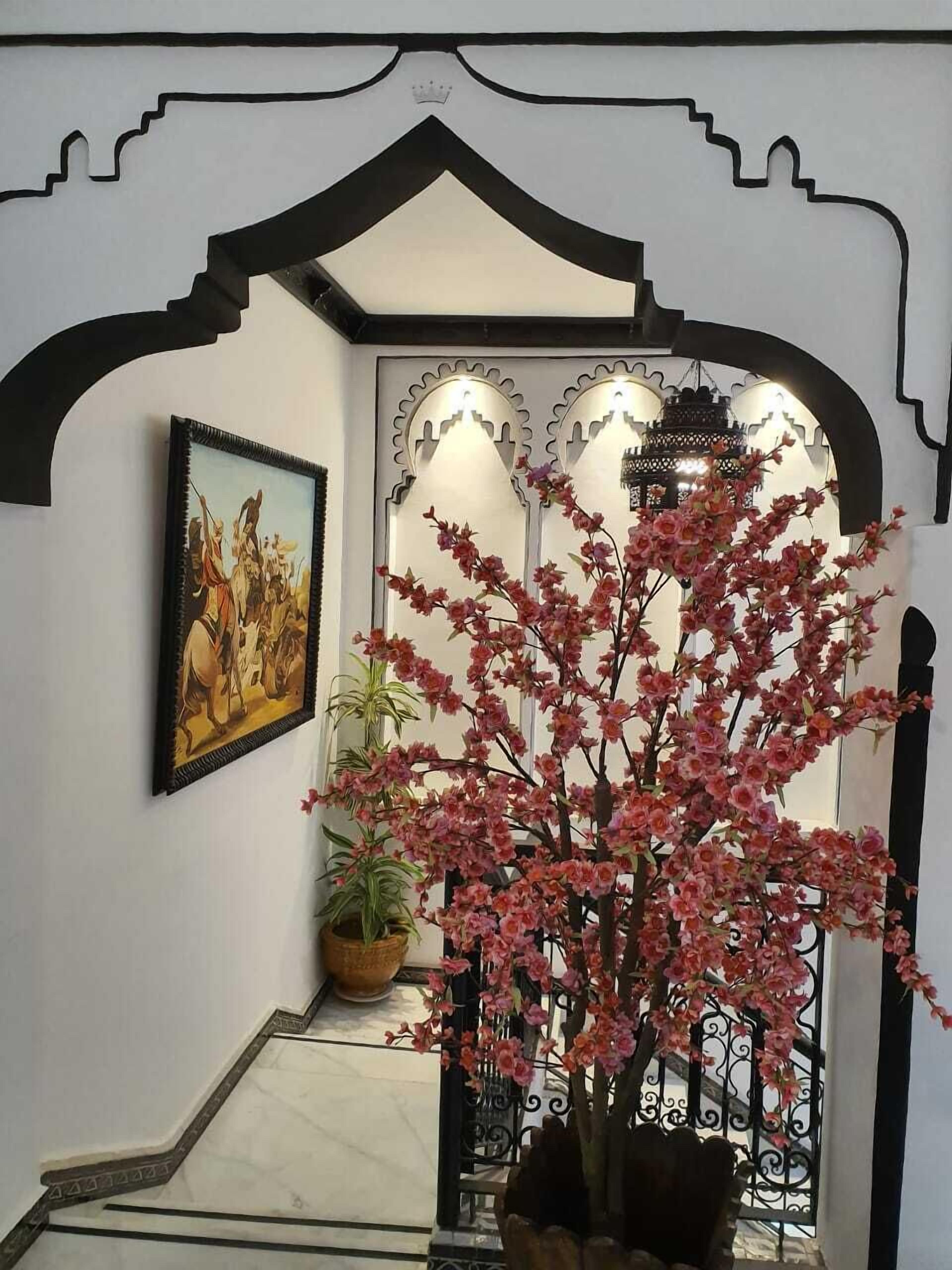 A hallway with a decorative archway, a framed painting, and a potted plant with pink flowers.