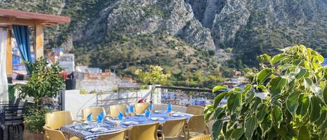Un área de comedor al aire libre con mesas y sillas, con vistas a un paisaje montañoso.