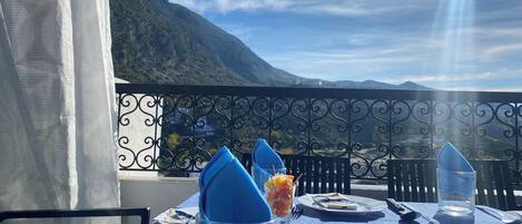 A table set for two with a mountain view, a blue tablecloth, and a glass of water.