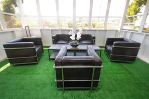 A room with a green artificial turf floor, a central coffee table, and four dark-colored sofas arranged around it. - Home Sweet Home Amboy (North Little Rock)