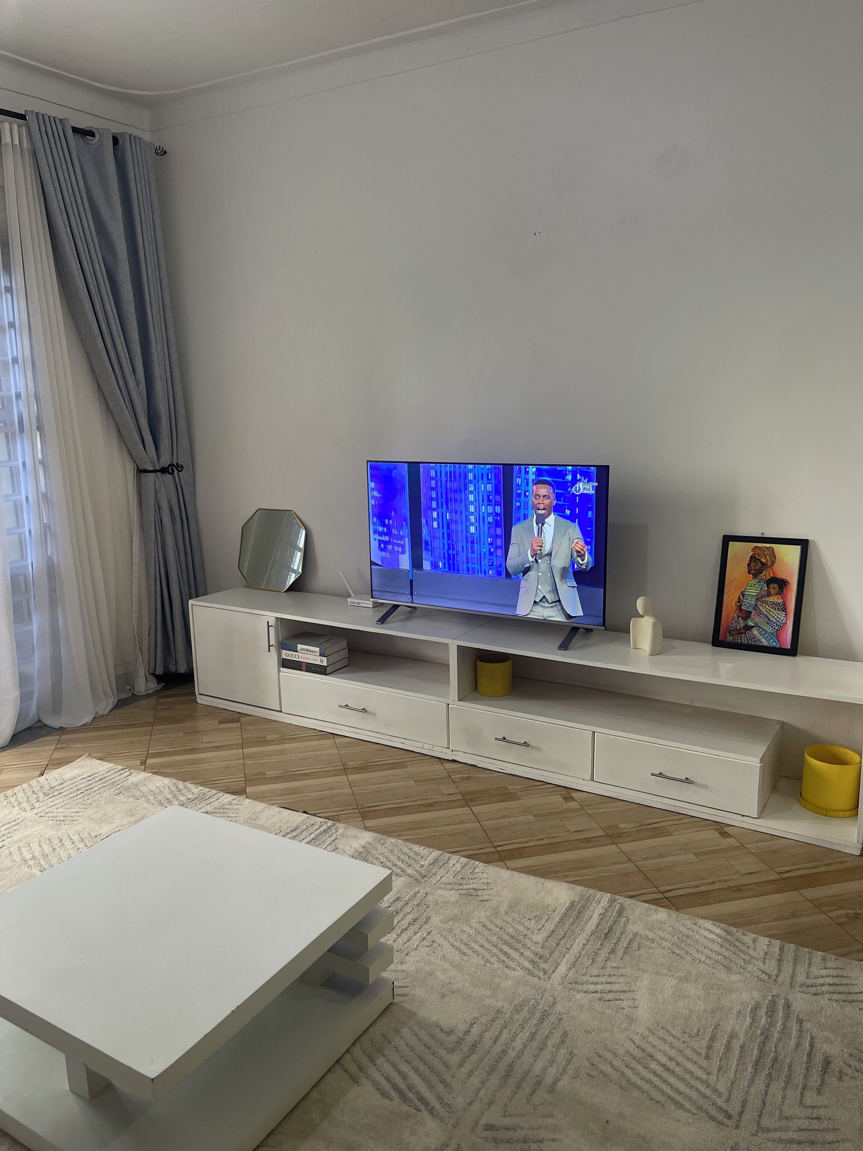 Un salon moderne avec un téléviseur à écran plat posé sur un meuble de télévision blanc, une table basse blanche et un tapis à motifs.