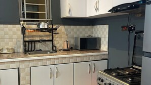 A modern kitchen with white cabinets, a gas stove, a microwave, and a window with blinds. - Cozy amazing one bedroom unit Mariam  (Kampala)