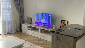 A modern living room with a flat-screen TV, a white coffee table, a patterned rug, and a kitchen island with a tiled backsplash. - Cozy amazing one bedroom unit Mariam  (Kampala)