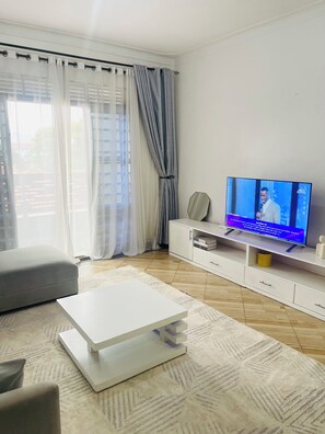 A modern living room with a flat-screen TV, a white entertainment unit, a grey sofa, and a patterned rug. - Cozy amazing one bedroom unit Mariam  (Kampala)