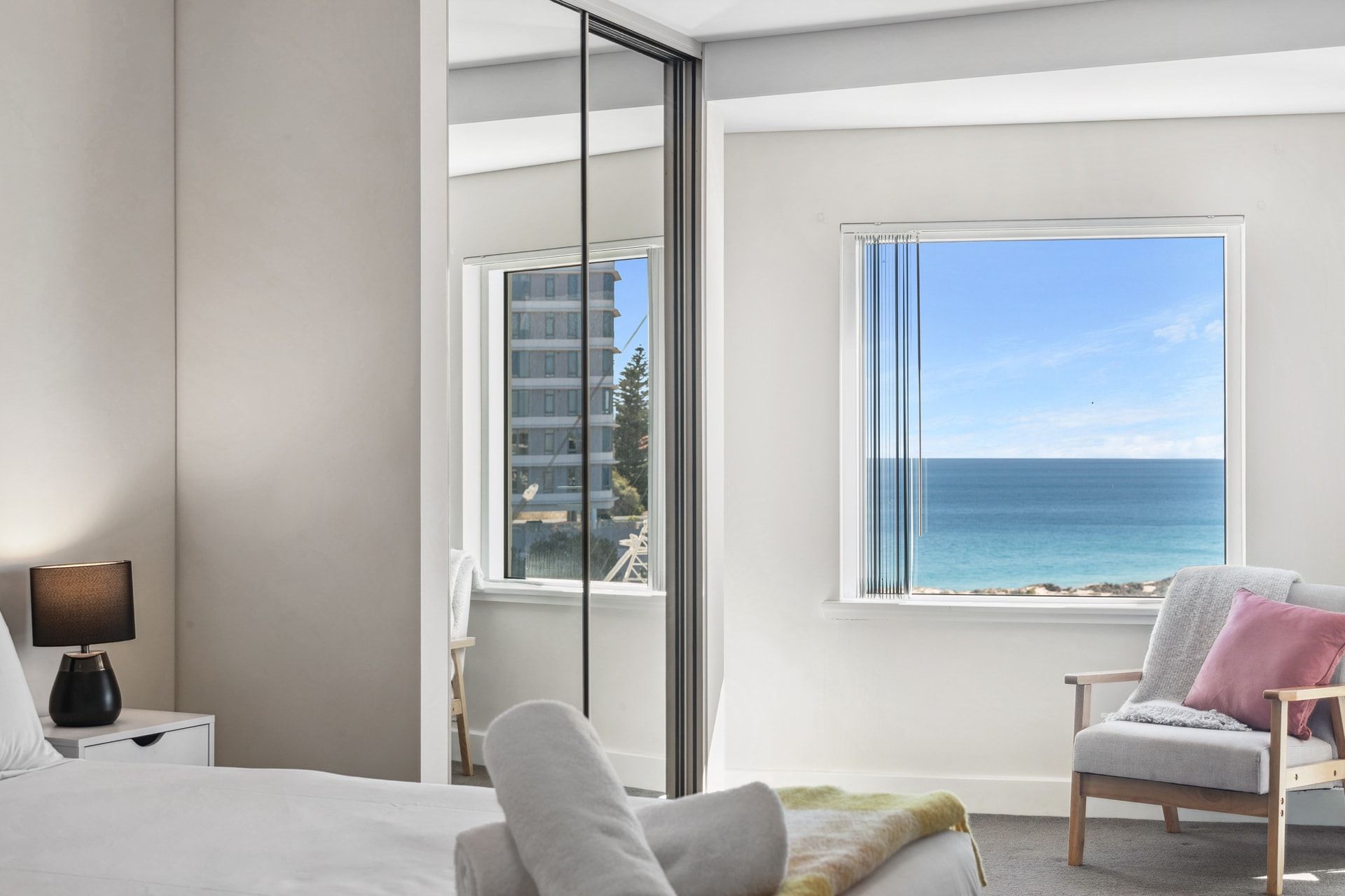 A bedroom with a bed, a chair, a nightstand, and a window with a view of the ocean.
