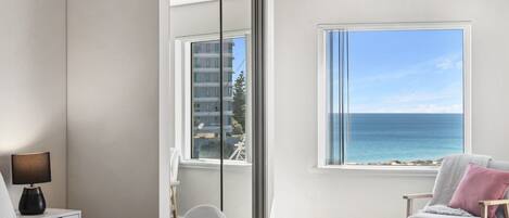 A bedroom with a bed, a chair, a nightstand, and a window with a view of the ocean.