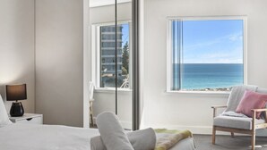 A bedroom with a bed, a chair, a nightstand, and a window with a view of the ocean.
