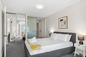 A hotel room with a large bed, a bedside table, a lamp, and a painting on the wall. - Apartment R311 - smart, stylish apartment in resort complex (Scarborough)